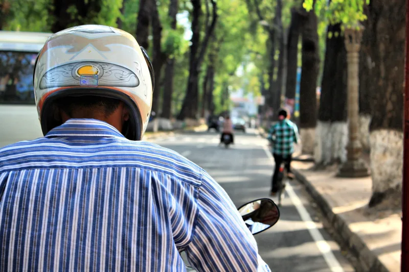 A motorbike rider in a striped shirt and helmet travels down a tree-lined street in Siem Reap.