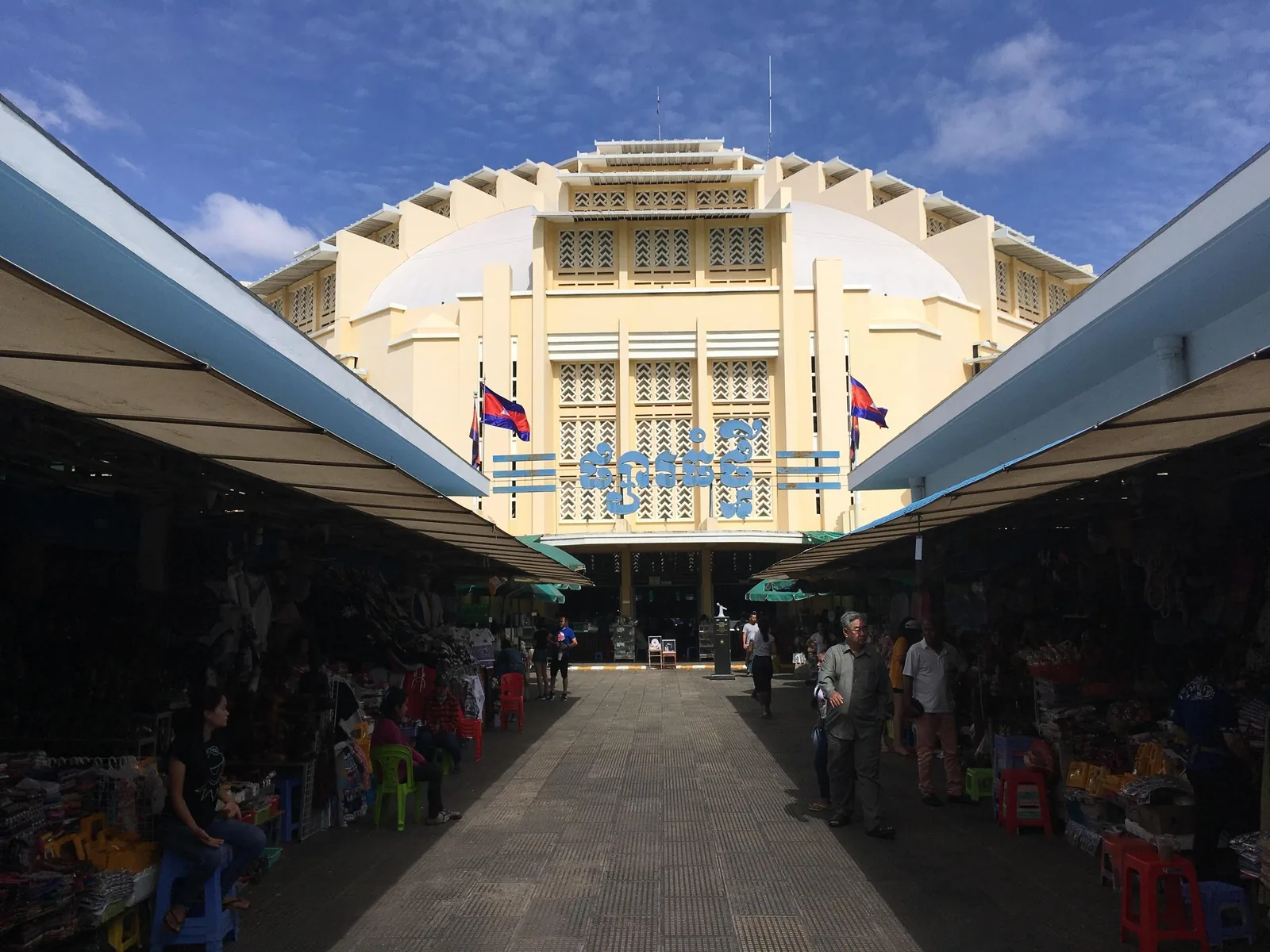 The art deco dome of Phnom Penh's Central Market rises above rows of covered vendor stalls under a blue sky.