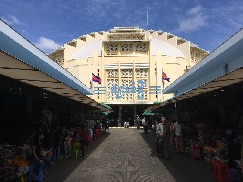The art deco dome of Phnom Penh's Central Market rises above rows of covered vendor stalls under a blue sky.