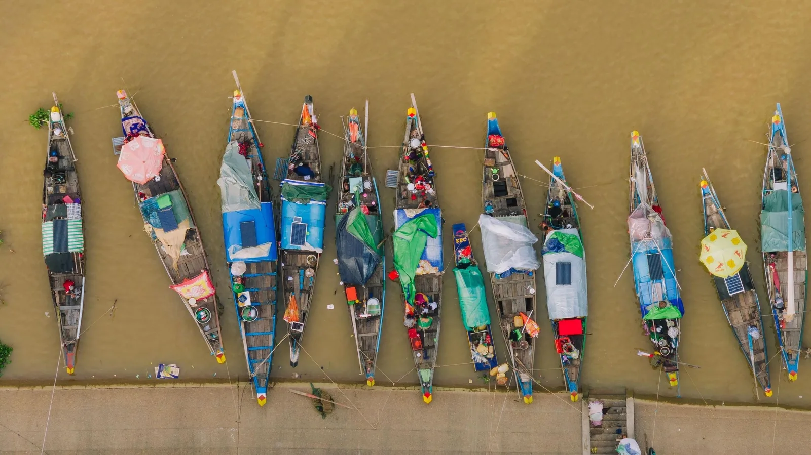 Aerial view of colorful wooden boats moored side by side along a muddy riverbank in Cambodia