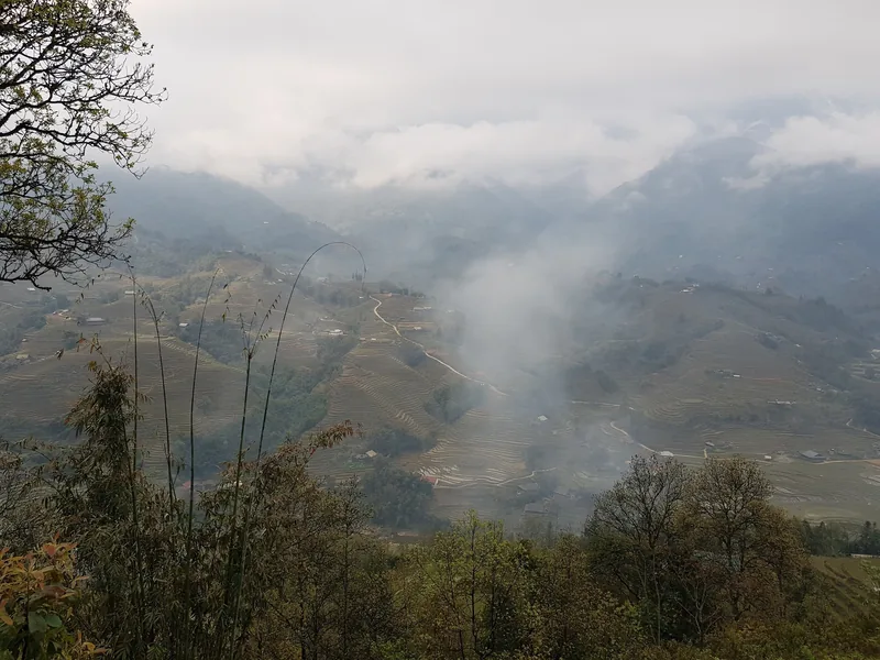 Mist drifts over terraced rice fields and mountain slopes near Sapa, Vietnam.