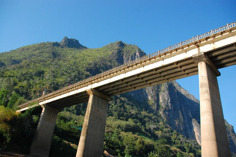 An elevated concrete bridge spans a valley beneath jagged limestone peaks near Nong Khiaw, Laos.